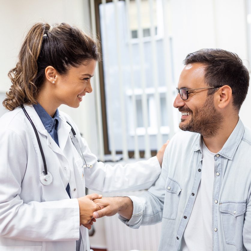 Young woman doctor or GP in white medical uniform consult male patient in private hospital. Female therapist speak talk with man client on consultation in clinic.